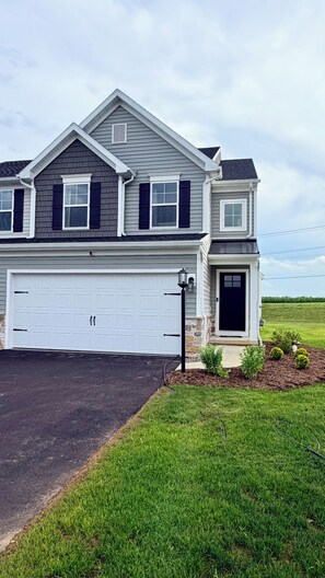 A two-story residential house with a garage, a front porch, and a landscaped yard. - New 3BR/3.5BA end unit townhouse under 3.5 mi from Beaver Stadium-full basement (State College)