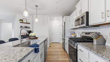 A modern kitchen with granite countertops, stainless steel appliances, and pendant lighting.