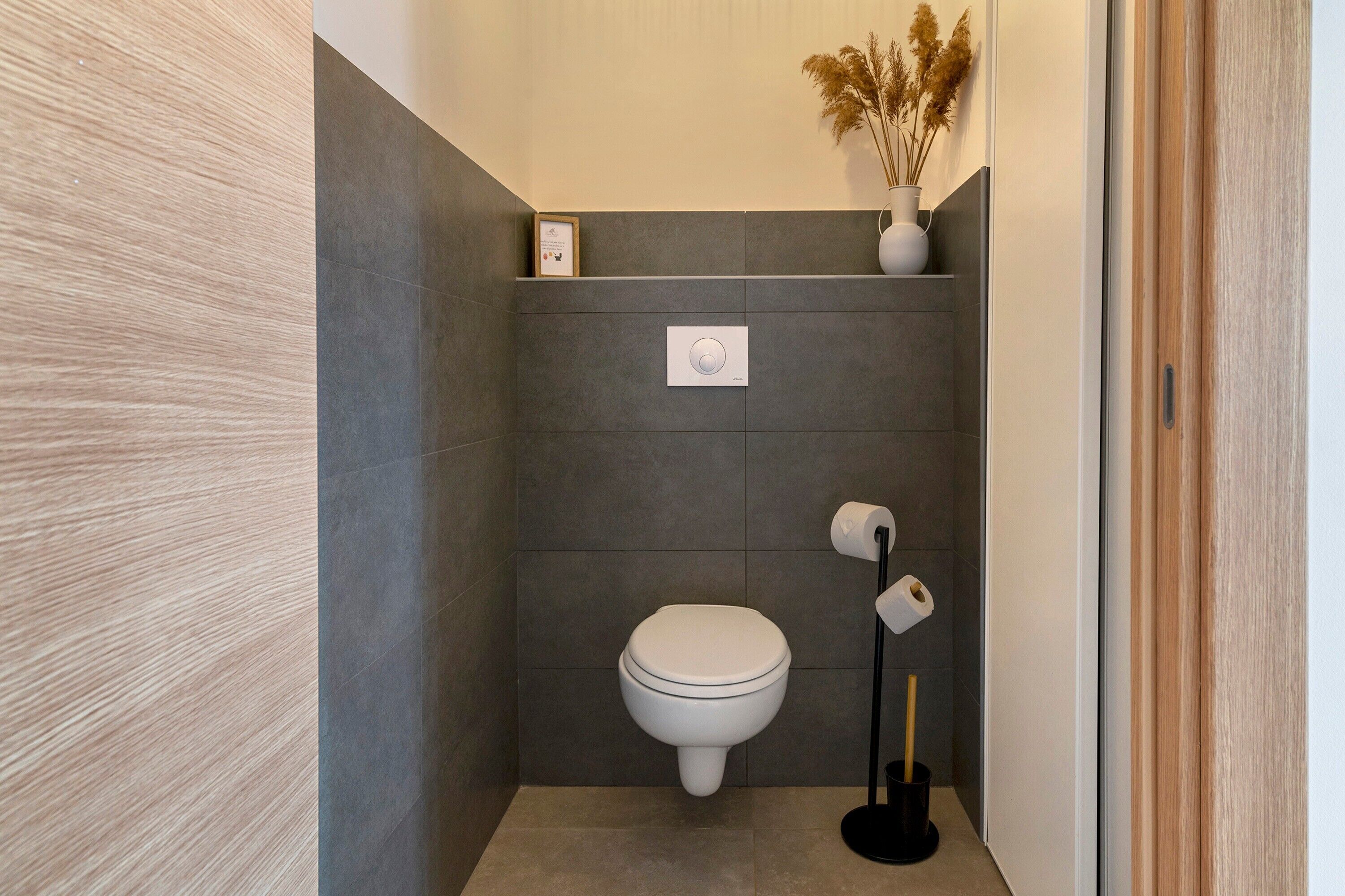 Een moderne badkamer met een toilet, een bedieningsplaat aan de muur en een toiletrolhouder.