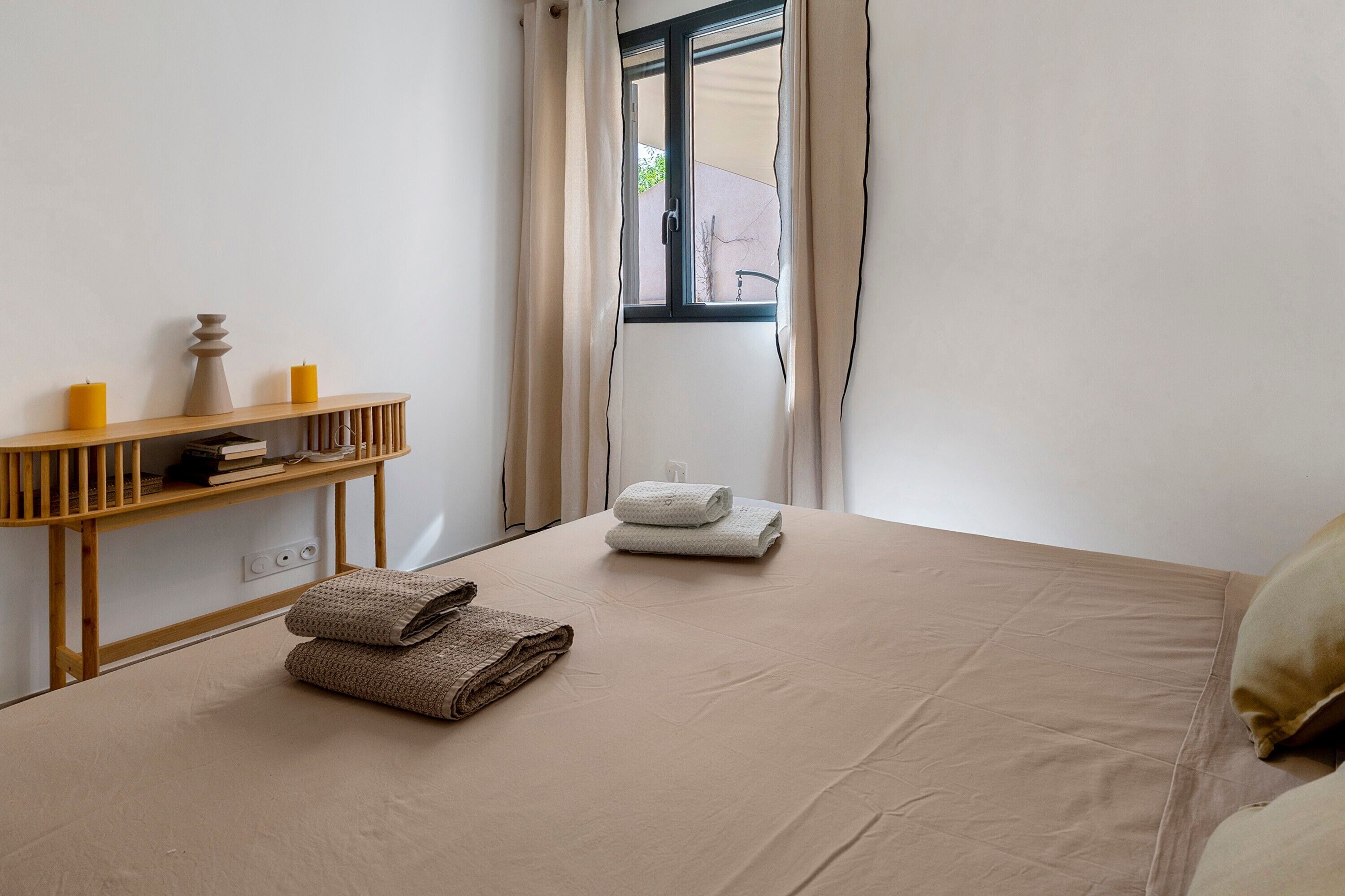 A room with a bed, a wooden console table with candles, and a window with curtains.