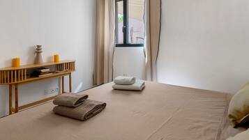 A room with a bed, a wooden console table with candles, and a window with curtains.