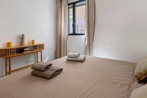 A room with a bed, a wooden console table with candles, and a window with curtains.