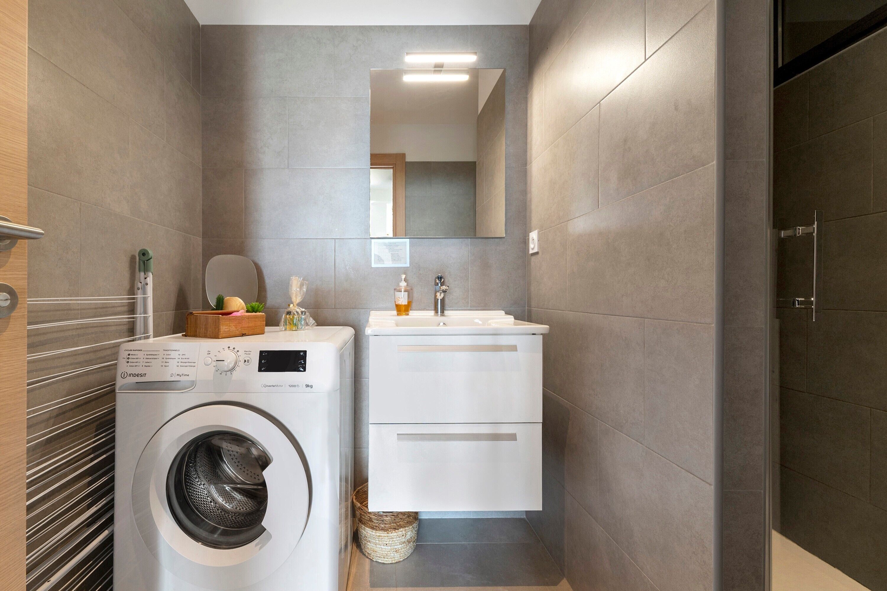 A compact laundry room with a front-loading washing machine, a sink, and a mirror above the counter.
