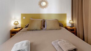 Un lit bien fait, avec une tête de lit, deux lampes de chevet et un luminaire fixé au mur.
