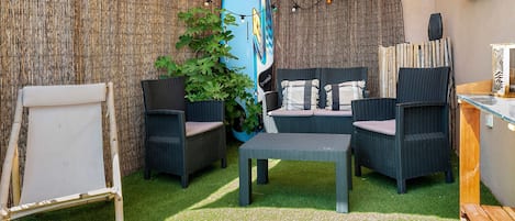 A cozy outdoor seating area with wicker furniture, a surfboard decoration, and string lights.