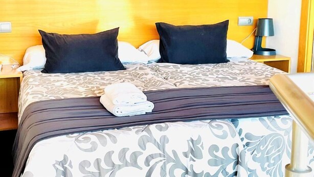 A hotel room with a bed, two pillows, a nightstand with a lamp, and a folded towel on the bed. - La Perla Reyes Catolicos Living: Standard Apartment (Granada)