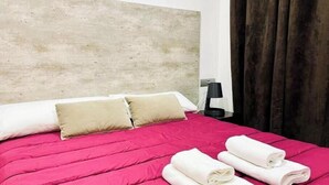 A hotel room with a bed, pillows, a nightstand, a lamp, and a window with curtains. - La Perla Reyes Catolicos Living: Standard Apartment (Granada)