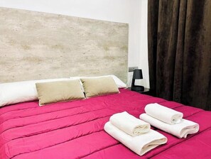 Ein Hotelzimmer mit einem Bett, Kissen, einem Nachttisch, einer Lampe und einem Fenster mit Vorhängen.