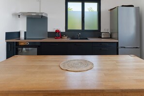 A modern kitchen with a wooden table, a red coffee maker, a toaster, and a refrigerator.