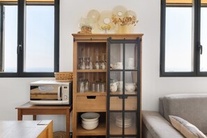A kitchen with a microwave, a wooden cabinet with glass doors, and a view of the outdoors through the windows.