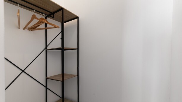 A corner of a room with a black metal shelving unit with three shelves and a wooden bench.