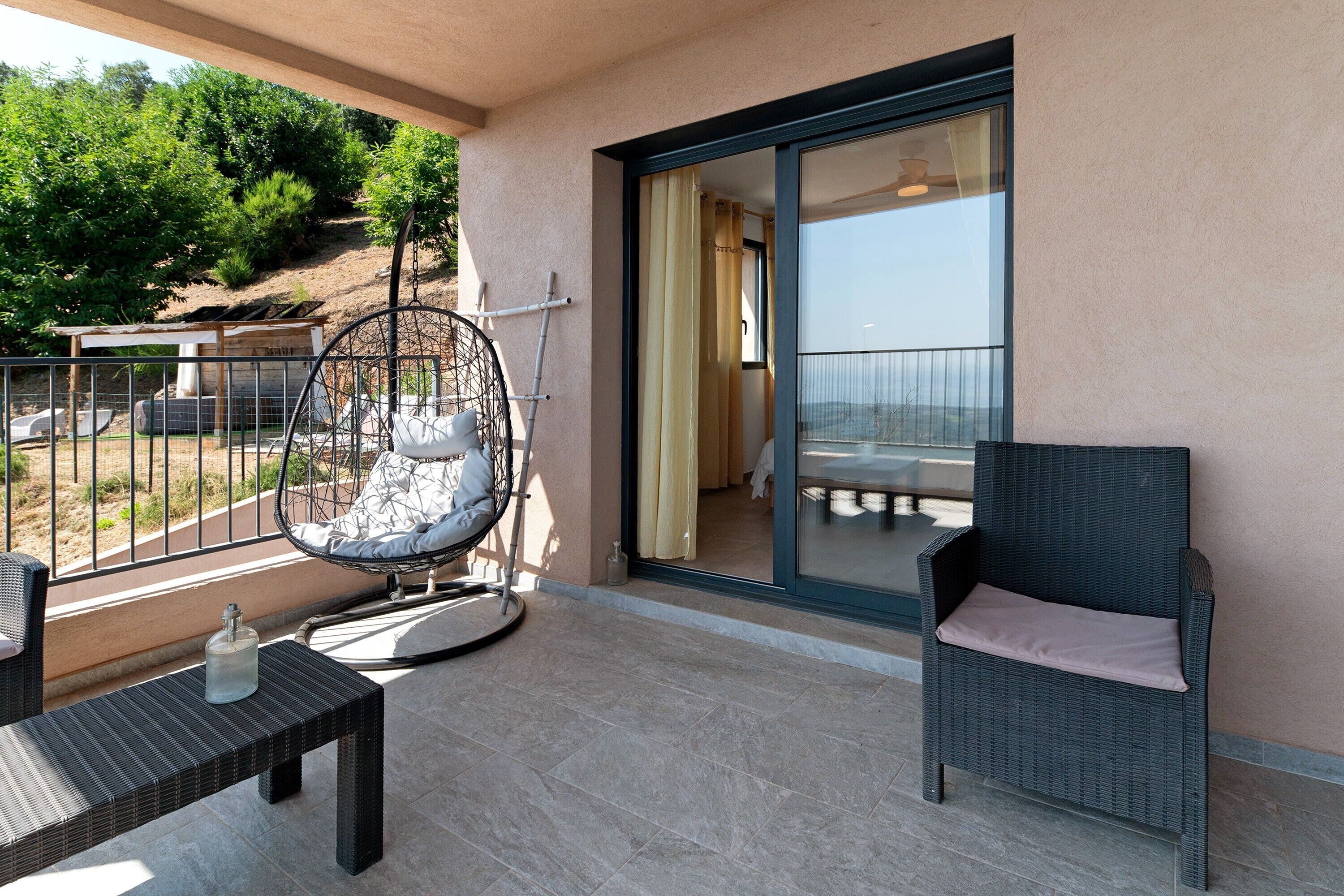 A balcony with a wicker chair, a table, and a glass door leading to an indoor area.