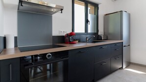 A modern kitchen with a built-in oven, a dishwasher, a red coffee maker, and a stainless steel refrigerator.