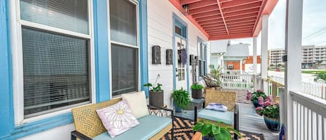 A covered porch with a seating area, potted plants, and a view of the surrounding buildings.