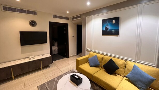 Een moderne woonkamer met een bank, een salontafel, een televisie en een schilderij aan de muur.