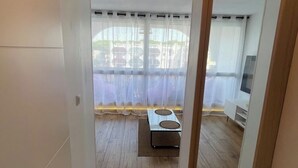 Un couloir étroit au plancher de bois, une porte cintrée peinte en blanc et une vue sur un balcon avec une table et des chaises.
