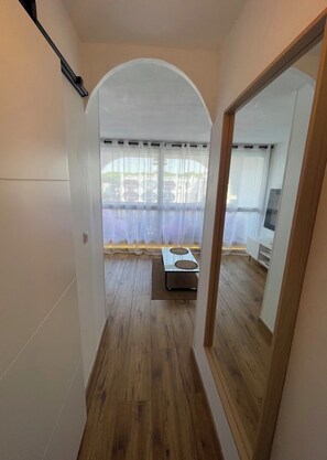 A narrow hallway with wooden flooring, a white arched doorway, and a view of a balcony with a table and chairs. - Charming studio in marvelous La Grande-Motte with AC comfort (La Grande-Motte)