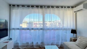 Un salon comprenant un téléviseur, un canapé, une table basse et une grande fenêtre ornée de rideaux légers.