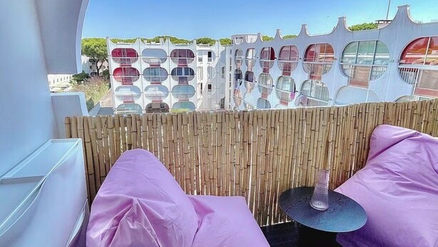 Un intérieur lumineux, baigné de soleil, avec vue sur une rangée de bâtiments modernes aux couleurs vives.