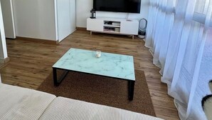Un salon moderne doté d’un téléviseur à écran plat, d’un meuble de rangement blanc, d’une table basse en marbre et d’un canapé à rayures.