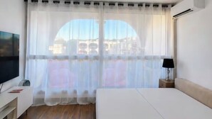 Une chambre d’hôtel avec un lit, une télévision, une lampe et une fenêtre avec des rideaux légers.
