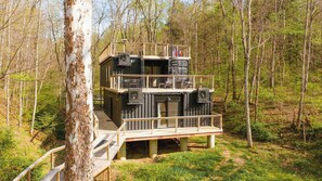 A multi-level cabin with a balcony, surrounded by trees. - Unique Container Retreat With Creek Villa (McArthur)
