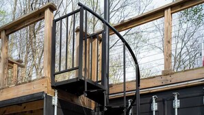 A spiral staircase leading to a wooden deck, a garage door, and a metal railing. - Unique Container Retreat With Creek Villa (McArthur)