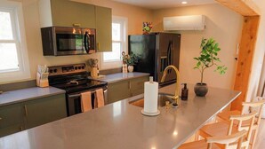 A modern kitchen with a large island, bar stools, and built-in appliances. - Unique Container Retreat With Creek Villa (McArthur)