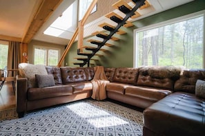 Una sala de estar moderna con un amplio sofá de cuero marrón en forma de L, un tapete estampado y una escalera de madera.