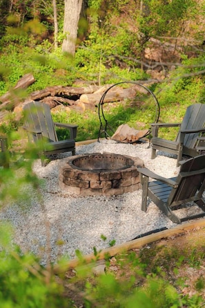 Un hogar con leña rodeado de grava y vegetación, con dos sillas Adirondack.