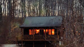 A cabin with a porch, a dirt path leading to it, and a forested background. - Secluded Cozy Log Cabin Villa (McArthur)
