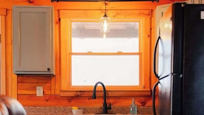 A kitchen with wooden cabinets, a black refrigerator, a window with a light fixture, and a countertop. - Secluded Cozy Log Cabin Villa (McArthur)