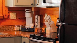 A kitchen with wooden cabinets, a coffee maker, a microwave, and a knife block. - Secluded Cozy Log Cabin Villa (McArthur)