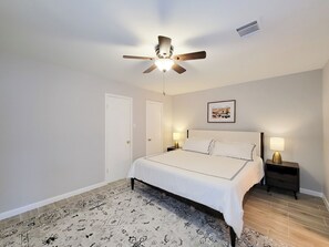 A bedroom with a bed, two bedside tables with lamps, a ceiling fan, a door, and a wall-mounted picture. - Bright, Modern Lakefront 3 Bedroom Townhouse (Montgomery)