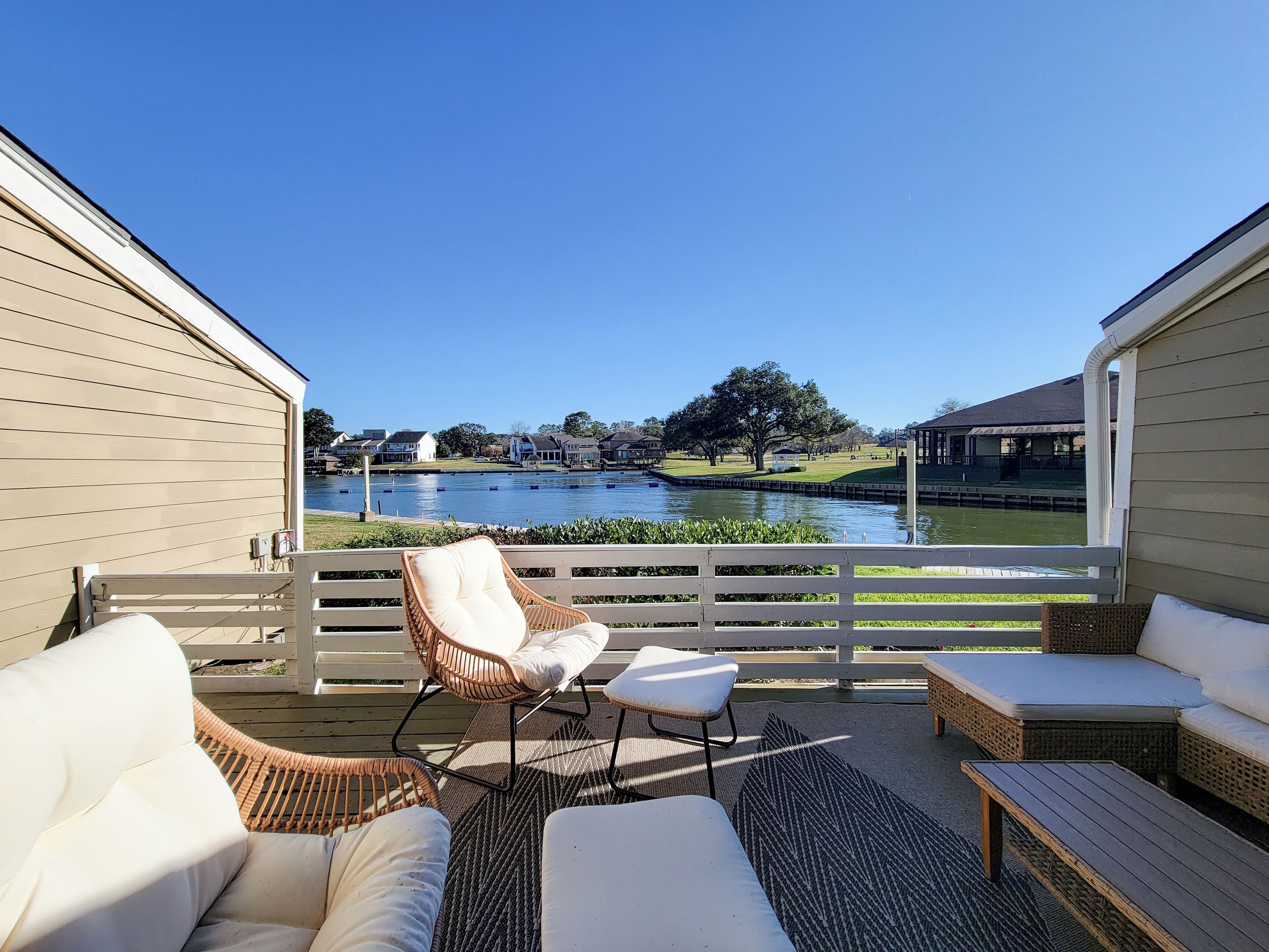 A covered outdoor seating area with wicker furniture and a view of a lake and buildings.