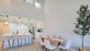 A modern kitchen with white cabinets, a central island with bar stools, and a dining area with a wooden table and white chairs.