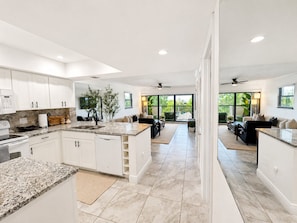 A modern kitchen with white cabinets, granite countertops, and a dining area with a large window overlooking a green landscape. - Park Shore Resort - Dream Holiday Stays (Naples)