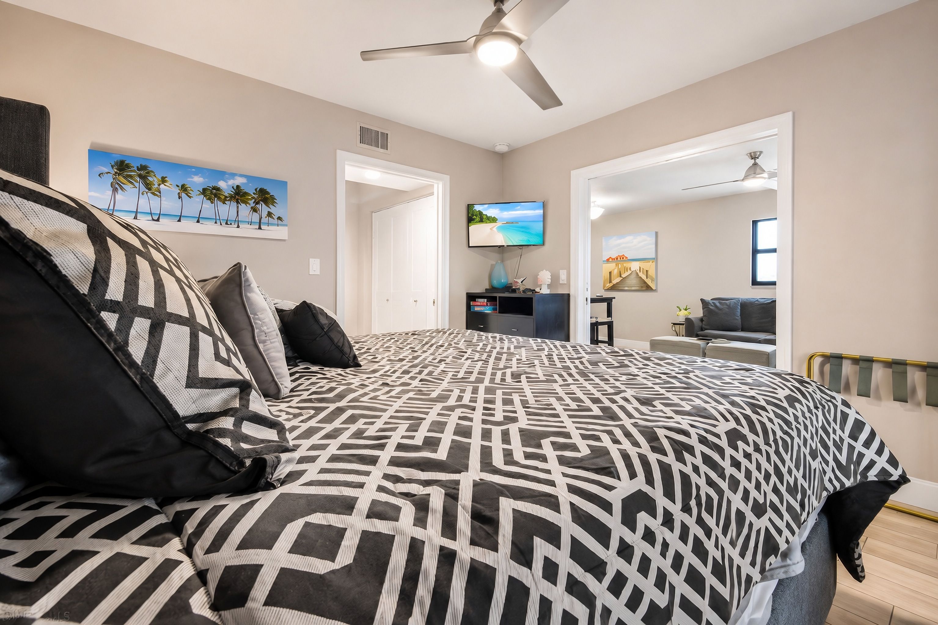 A bedroom with a bed, a ceiling fan, a TV, and a door leading to another room.