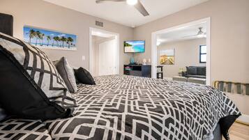 A bedroom with a bed, a ceiling fan, a TV, and a door leading to another room.