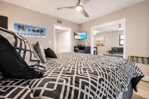 Quarto com cama, ventilador de teto, televisão e porta para outro cômodo.