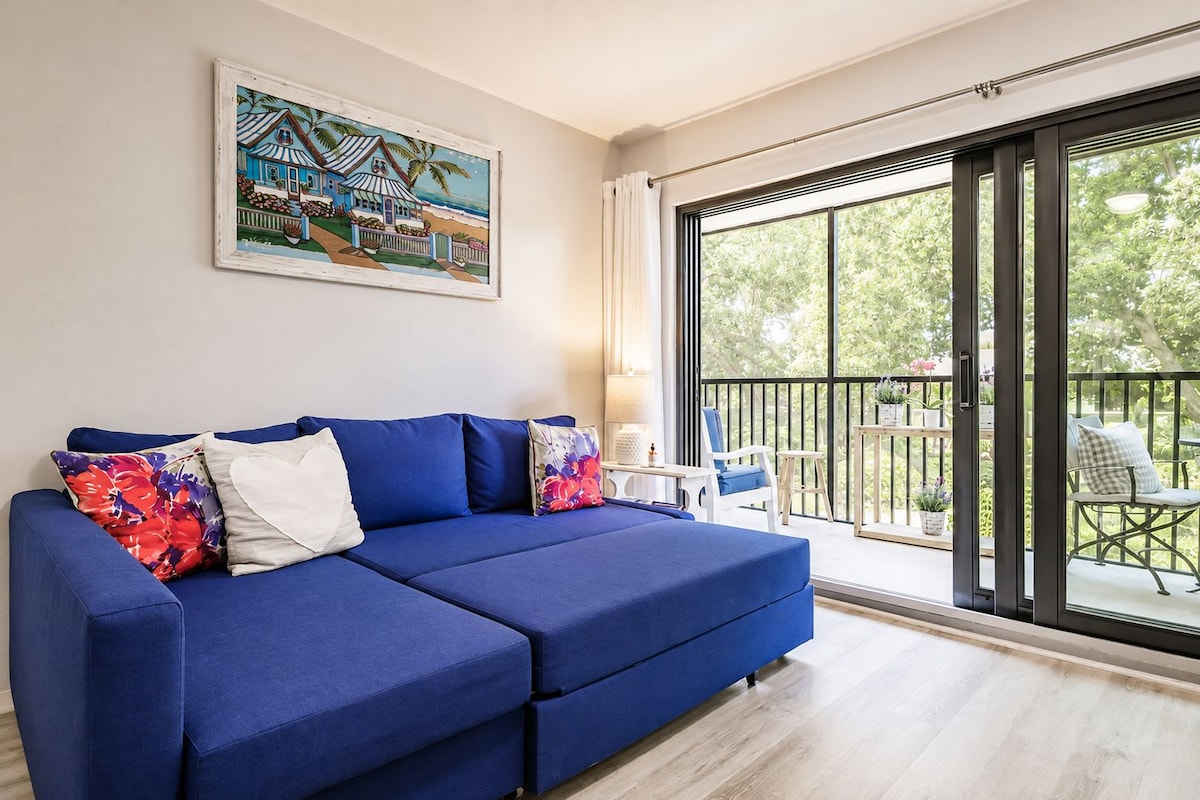 Uma sala de estar moderna com um sofá azul, uma pintura e uma varanda com mobiliário de exterior.