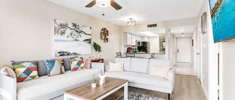 Un salon moderne avec un canapé blanc, des coussins colorés, une table basse en bois et un ventilateur de plafond.