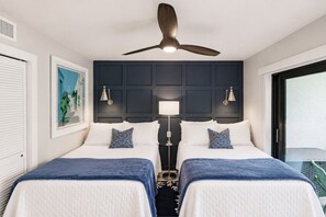 A hotel room with two beds, a ceiling fan, a nightstand with lamps, a framed picture on the wall, and a view through a glass door. - Park Shore Resort - Dream Holiday Stays (Naples)