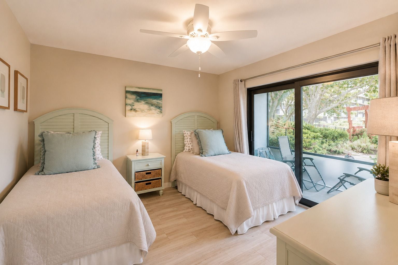 A bedroom with two beds, a ceiling fan, a nightstand with a lamp, and a window with a view of the outdoors.