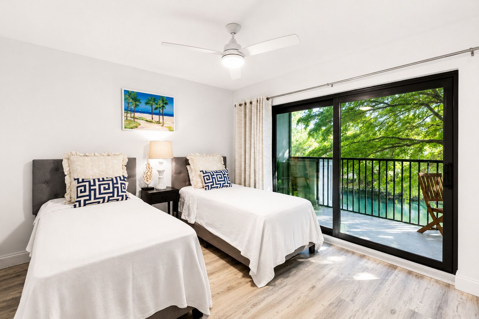 A bedroom with two beds, a ceiling fan, a window with a view of greenery, and a chair by the window.