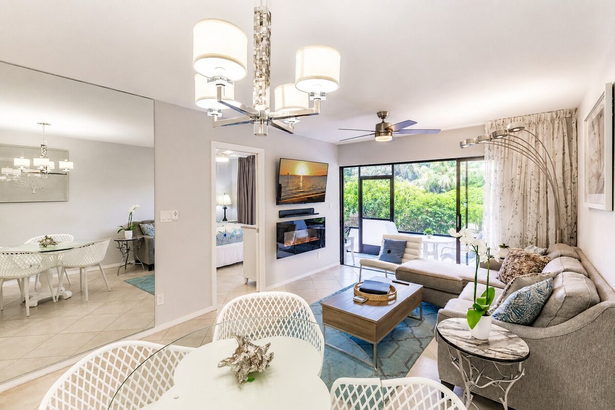 Sala de estar moderna com área de jantar, sofás, televisão e varanda com vista para o verde.
