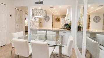 A modern kitchen with a glass dining table, white chairs, and a large mirror.
