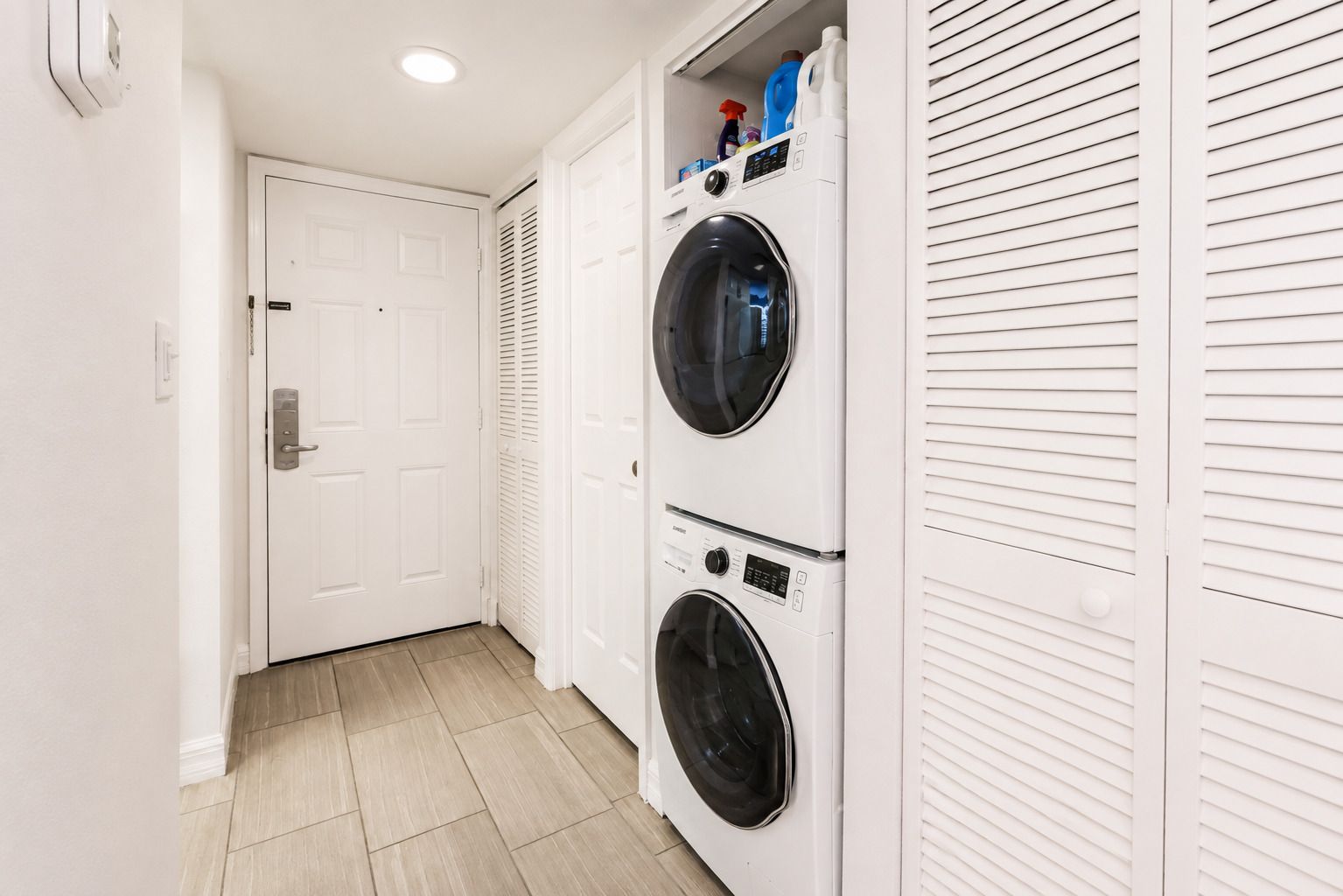 A laundry room with two stacked front-loading washing machines, a white door, and a vented wall.