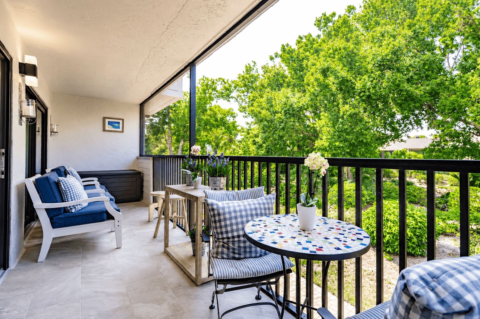 A balcony with a seating area, a table, and potted plants.