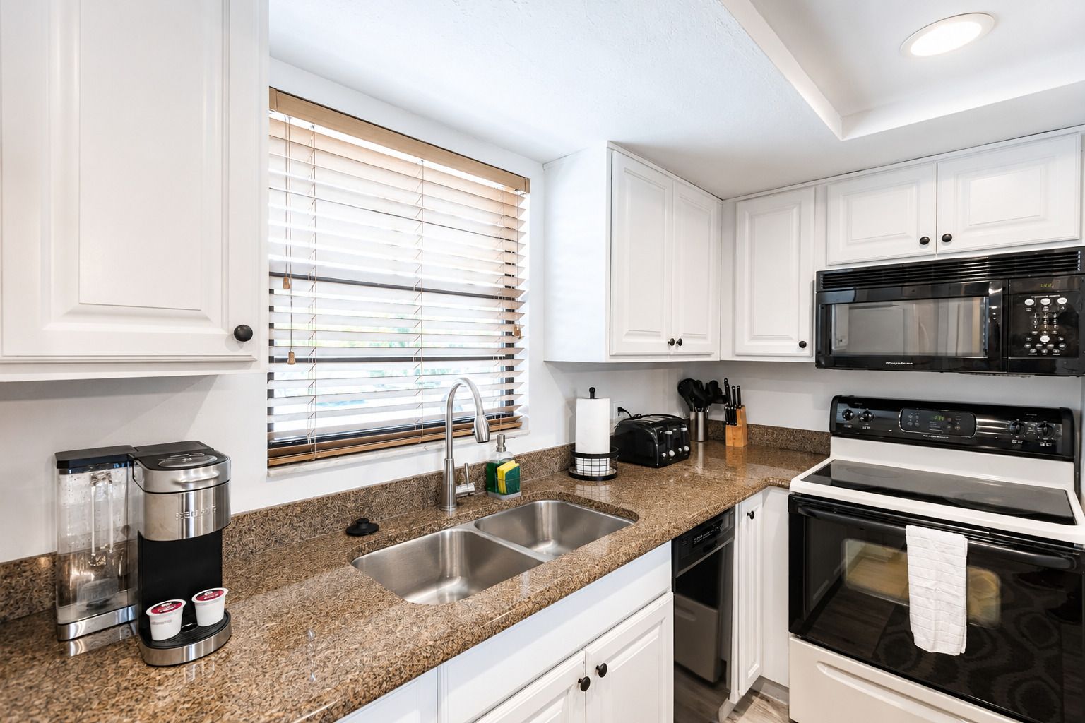 A modern kitchen with white cabinets, a granite countertop, a coffee maker, a toaster, a microwave, and an oven.